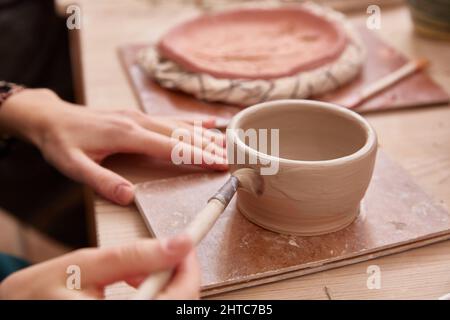 Gesichtslose Frau malt eine Tonschale. Nahaufnahme. Stockfoto