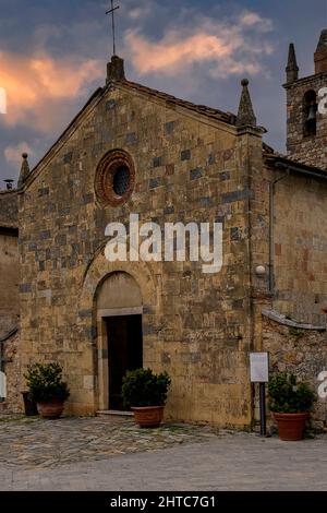 Ein runder oculus, umrahmt von geformtem Terrakotta, durchdringt die goldene romanische Fassade der Chiesa di Santa Maria Assunta Anfang 1200s auf der Piazza Roma, Monteriggioni, Toskana, Italien. Stockfoto