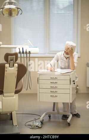 Eine Zahnärztin füllt Papierkram aus, während sie an einem Schreibtisch in ihrem Büro sitzt. Stockfoto