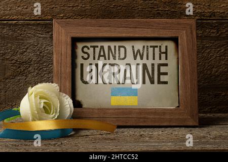 Holzrahmen mit Textständer für die Ukraine auf Holztisch mit einer weißen Rose und zwei Bändern mit ukraine-Flagge Farbe Stockfoto