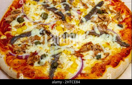 Thunfisch, Sardellen, Mais, Kaper und Pizza mit roten Zwiebeln Stockfoto
