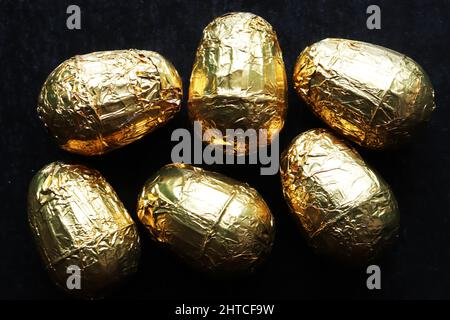 Schuss von sechs Schokolade Ostereiern in Goldfolie auf Schieferhintergrund eingewickelt Stockfoto