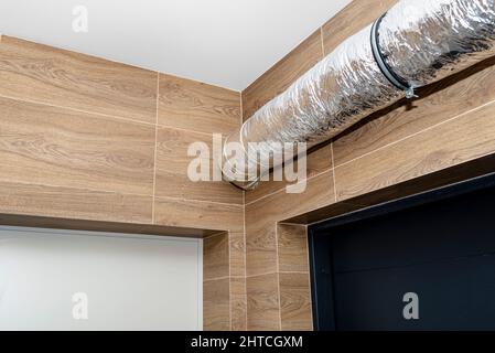 Lufteinlass und -Abluft in der Wohnung mechanische Belüftung mit Wärmerückgewinnung mit sichtbaren isolierten Rohren mit Silberfolie in die Wand eindringen. Stockfoto