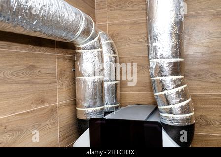 Lufteinlass und -Abluft in der Wohnung mechanische Belüftung mit Wärmerückgewinnung mit sichtbaren isolierten Rohren mit Silberfolie. Stockfoto