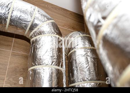 Lufteinlass und -Abluft in der Wohnung mechanische Belüftung mit Wärmerückgewinnung mit sichtbaren isolierten Rohren mit Silberfolie in die Wand eindringen. Stockfoto