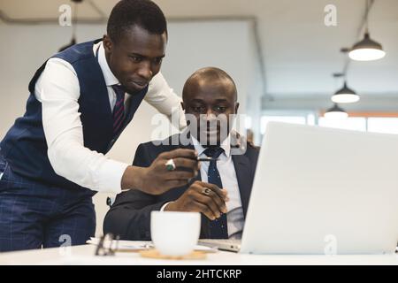 Zwei afroamerikanische Geschäftspartner arbeiten gemeinsam an einem Laptop an einem gemeinsamen Projekt. Gegenseitige Unterstützung und Aufbau sozialer Kontakte Stockfoto