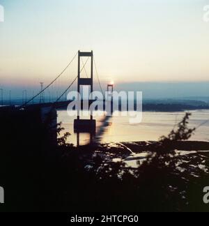 Severn Bridge, M48, Aust, South Gloucestershire, 1987-1989. Die Severn-Brücke bei Sonnenuntergang, gesehen während der von Laing geleisteten Verstärkungsarbeiten. Das ursprüngliche Design und der Bau der Severn-Brücke hatten das erhöhte Verkehrsaufkommen seit ihrer Fertigstellung im Jahr 1966 unterschätzt, und obwohl es auf eine Lebensdauer von 120 Jahren gebaut wurde, wurde festgestellt, dass bereits nach 20 Sanierungsarbeiten erforderlich waren. Laing Industrial Engineering &amp; Construction gewann den &#XA3;29,5m-Vertrag vom Ministerium für Verkehr und Stärkung der Arbeit an allen Elementen der Struktur begann im Mai 1987. Das Projekt wurde im April 1990 im selben Jahr abgeschlossen Stockfoto