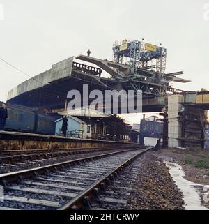 Westway Flyover, A40, Kensington and Chelsea, London, Oktober-Dezember 1969. Der Transporterkran senkt eine Deckeinheit des Westway Flyover an ihren Platz, während er die Eisenbahn in der Nähe der Westbourne Park Station überspannt. Der Transporterkran wurde speziell von der Laing-Werksabteilung entworfen und gebaut. Die vierbeinige Gantry machte 400 Fahrten entlang der Fahrbahn von Abschnitt 5, hob die einzelnen Decks vom Ende der Harrow Road an, transportierte sie auf der Länge der Autobahn und senkte sie in Position. Die Deckseinheiten für Abschnitt 5 wiegen bis zu 130 Tonnen und sind mehr als 28 Meter breit und tragen al Stockfoto