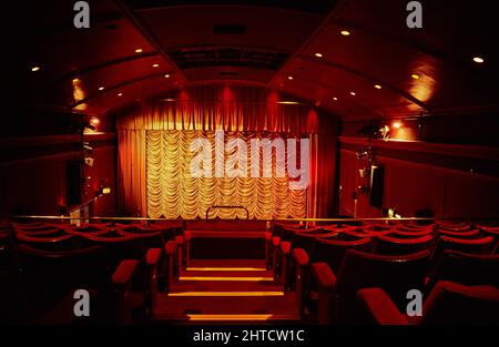 Metro Cinema, Shrewsbury Road, Penistone, Barnsley, South Yorkshire, 1999-2002. Blick entlang des Mittelganges zwischen den Sitzen im Kreis auf die mit einem Vorhang besäumte Leinwand im Auditorium des Metro Cinema. Das Rathaus von Penistone oder die Versammlungshalle und Bibliothek wurde 1913 erbaut. Das Gebäude wurde um 1915 als Kino in Betrieb genommen und im Jahr 1920s wurde das Kino erweitert. 1986 wurde es in Metro Cinema umbenannt; zu diesem Zeitpunkt war das Rathaus in die ehemalige Bibliothek im westlichen Ende des Gebäudes umgezogen. Anfang des 21.. Jahrhunderts wurde das Kino als Penistone Paramount Cinema bekannt. Stockfoto