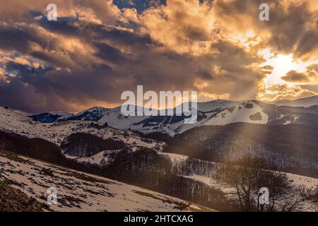 Goldene Lichter bei Sonnenuntergang auf den schneebedeckten Gipfeln der Abruzzen. Wolkiger Himmel. Roccaraso, Provinz L'Aquila, Abruzzen, Italien, Europa Stockfoto