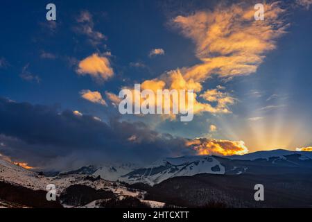 Goldene Lichter bei Sonnenuntergang auf den schneebedeckten Gipfeln der Abruzzen. Wolkiger Himmel. Roccaraso, Provinz L'Aquila, Abruzzen, Italien, Europa Stockfoto