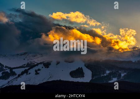 Goldene Lichter bei Sonnenuntergang auf den schneebedeckten Gipfeln der Abruzzen. Wolkiger Himmel. Roccaraso, Provinz L'Aquila, Abruzzen, Italien, Europa Stockfoto