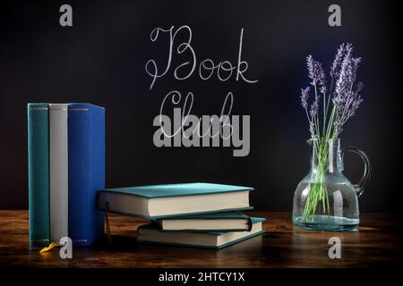 Club-Konzept Buchen. Ein Stapel Hardcover-Bücher mit Kreidebuchstaben auf einer Tafel und Lavendelblüten Stockfoto