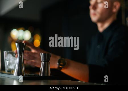 Blick aus der Perspektive des professionellen Barkeepers, der erfrischenden alkoholischen Cocktail zubereitet, hinter der Theke stehend, im Vordergrund auf Metalljigger fokussiert. Stockfoto