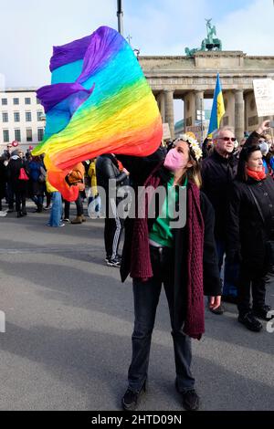 Frau in Gesichtsmaske mit Regenbogenfahne, Friedenssymbol. Menschen mit ukrainischen Fahnen und Plakaten protestieren gegen den Krieg in der Ukraine Stockfoto
