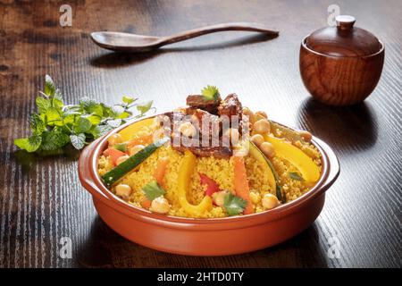 Fleisch- und Gemüsesorten Couscous, traditionelle marokkanische Küche, mit frischem Koriander und Minze. Festliches arabisches Gericht auf einem dunklen rustikalen Holztisch Stockfoto