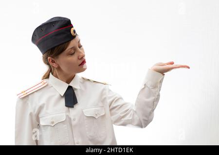 Schöne junge weibliche russische Polizist in Kleideruniform zeigt Schilder mit ihren Händen auf weißem Hintergrund. Selektiver Fokus. Hochformat Stockfoto