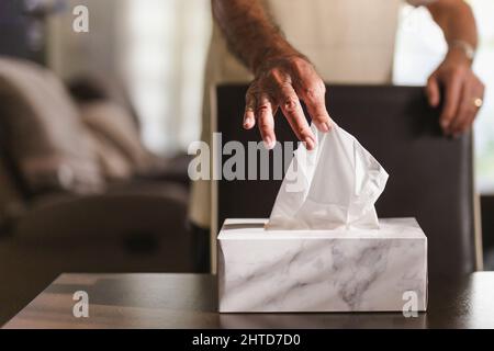 Ein älterer Mann nahm Seidenpapier von der Taschentuchbox auf dem Esstisch ab. Stockfoto