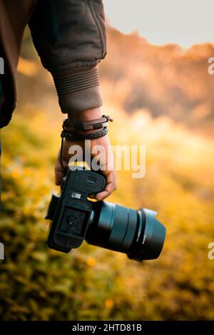 Der Fotograf hält eine Kamera, eine DSLR-Kamera mit unscharfem Hintergrundbild mit selektivem Fokus Stockfoto