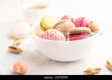 Bunte Makronen und Schokoladeneier in Keramikschale, Tasse Kaffee auf grauem Betongrund. Seitenansicht, Nahaufnahme, selektiver Fokus, Stillleben Stockfoto