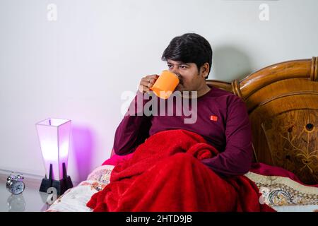 Junger Mann, der morgens im Schlafzimmer schlechten Kaffee trinkt - Konzept von Tagesablauf, Erfrischung und Selbstversorgung. Stockfoto