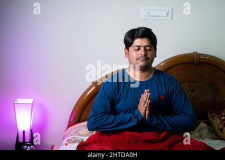 Junger Mann, der vor dem Schlafen die Hände auf dem Bett faltet und zu gott betet - Konzept des geistlichen Glaubens, des gesunden Schlafens und der Kontemplation Stockfoto