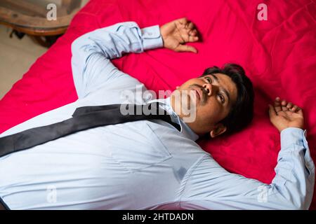 Blick von oben auf den müden jungen Geschäftsmann, der nach seiner Ankunft aus dem Büro ins Bett fiel - Konzept von überarbeiteter, gestresster und entspannender Atmosphäre. Stockfoto