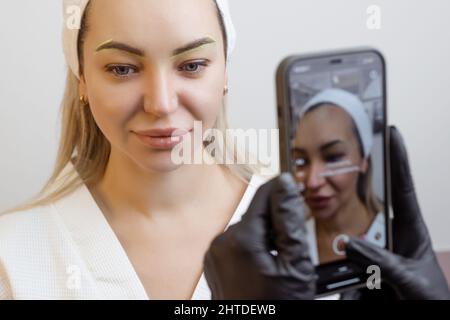 Dauerhaftes Make-up. Der Tattoo-Künstler fotografiert die Lippen eines Kunden auf seinem Telefon Stockfoto