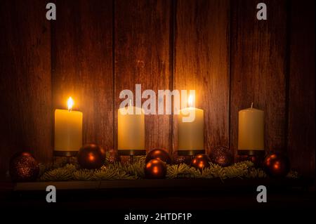 Eine ruhige Szenerie eines Adventsblumenarrangements mit vier brennenden Kerzen an einer Holzwand Stockfoto