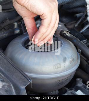 Ein Mann entschrauben den Ausgleichsbehälterdeckel eines Autos mit Kühlmittel, Nahaufnahme. Problem mit Überhitzung des Motors, Luftschleuse, System Stockfoto