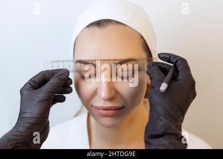 Augenbraue tätowieren.Permanent Augenbraue Make-up Master wendet die Kontur mit Faden auf die Augenbraue des Kunden Stockfoto