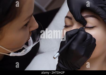 Dauerhaftes Make-up. Kosmetologe Tattoo Künstler wendet eine Kontur auf das Augenlid des Kunden für die anschließende Anwendung der Augen Tätowierung Stockfoto