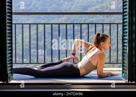 Junge Frau, die sich auf dem Balkon dehnt und ihre morgendliche Yoga-Routine macht Stockfoto