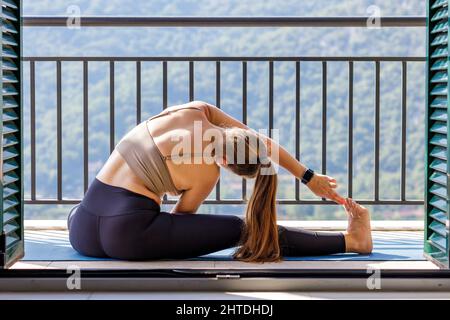 Junge Frau, die sich auf dem Balkon dehnt und ihre morgendliche Yoga-Routine macht Stockfoto