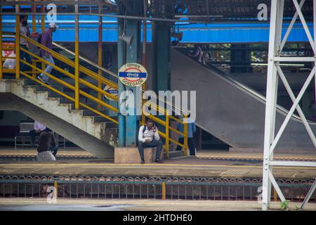 Mann, der am Bahnhof sitzt und eine Maske trägt und in Indien telefoniert Stockfoto