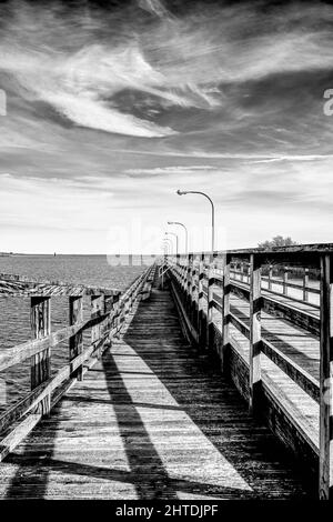 Vertikale Schwarz-Weiß-Aufnahme eines Piers und eines Wasserkörpers mit dunklen Wolken am Himmel Stockfoto