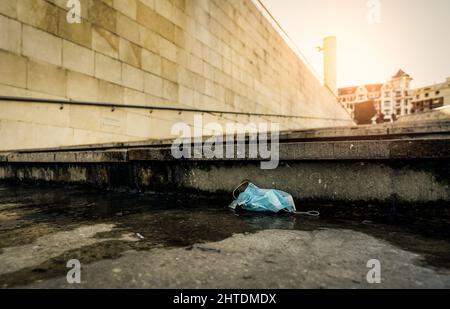 Gebrauchte medizinische Gesichtsmaske auf dem Boden auf Weichheit Gebäude in der Stadt entsorgen. Entsorgung von medizinischem Abfall mit unhygienischen. Schmutzige Stadt. Gesichtsmaske Abfall Müll Stockfoto