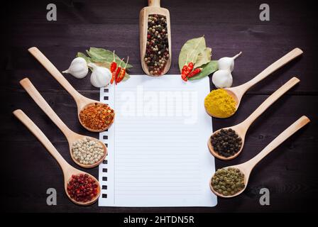Verschiedene exotische Gewürze in Löffel auf eine Holzplatte und leere White Paper für Rezepte Stockfoto