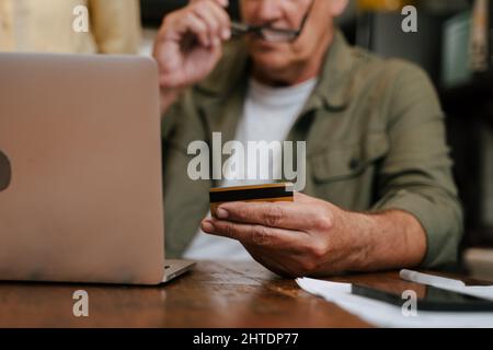 Nahaufnahme der Kreditkarte, während ältere Männer online von zu Hause aus einkaufen Stockfoto