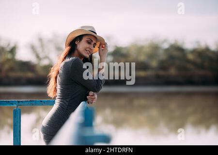 Lateinische Brünette Frau mit Hut auf einem Dock am Fluss entspannen. Konzept der Trennung in der Natur Stockfoto