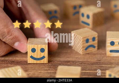 Hand pflücken lächelnd gesichtigen Holzwürfel und 5 Sterne. Symbol für die Überprüfung und Bewertung des Kundendienstes. Konzept Feedback zur Kundenzufriedenheit, Umfrage. Stockfoto