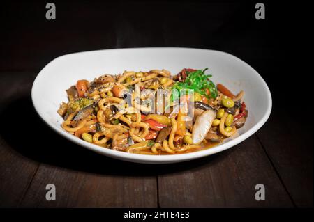 Asiatische vegetarische Gerichte udon-Nudeln mit Shiitake-Pilzen, Sesam und Pfeffer aus nächster Nähe auf einem Teller auf dem Holztisch. Hochwertige Fotos Stockfoto