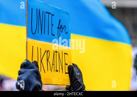 Toronto, Kanada - 27. Februar 2022: Ein Schild mit der Aufschrift "vereinigt euch für die Ukraine" gegen eine ukrainische Flagge. Die Kundgebung zur Unterstützung der Ukraine und gegen die Rus Stockfoto