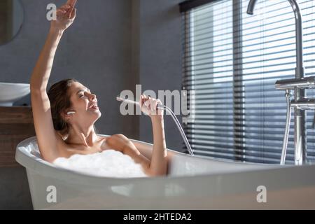 Fröhliche, Fröhliche Junge Frau, Die Sich In Der Schäumenden Badewanne Entspannt Und Singt Stockfoto