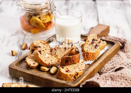 Kekse und Milch. Hausgemachte italienische Biscotti oder Cantuccini mit Mandeln und getrockneten Früchten auf weißem Holzhintergrund. Traditionelle italienische Kekse. Schließen Stockfoto