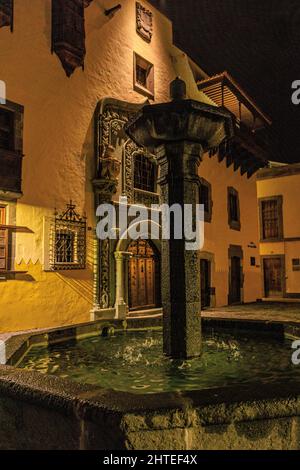 Wasser spritzt in den Steinbrunnen auf der plaza del pilar nuevo, der am frühen Abend von Las palmas gran canaria von Straßenlaternen beleuchtet wird Stockfoto