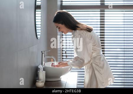 Schöne Junge Frau Trägt Weiße Seide Robe Waschen Gesicht Im Badezimmer Stockfoto