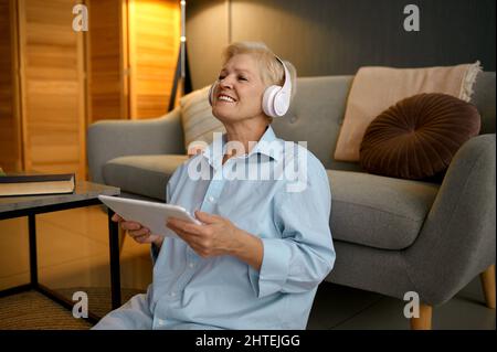 Ältere Frau, die mit einem Tablet Musik hört Stockfoto