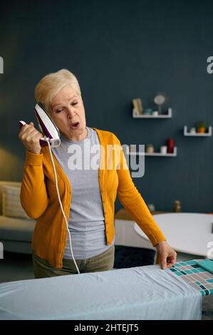 Die alte Frau war überrascht, dass sie sich bügelartig wie ein Telefon hielt Stockfoto