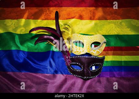 Zwei Karnevalsmasken mit Federn auf einer Gay Pride Flagge Stockfoto